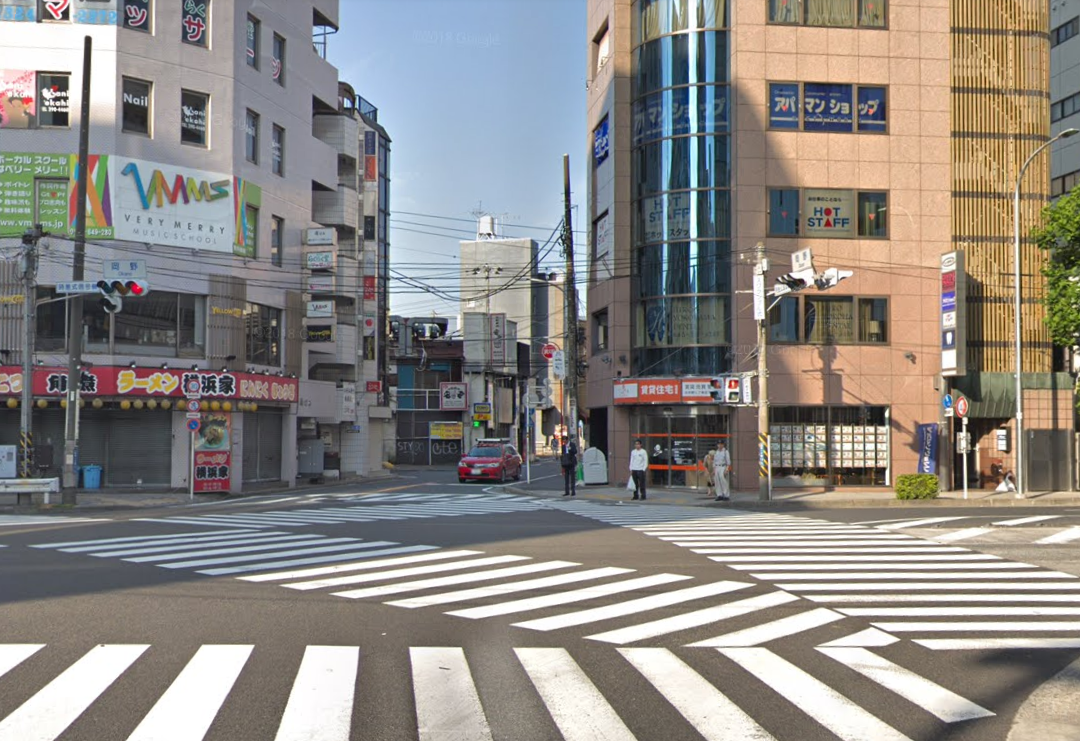 大きな交差点がございますので、信号を渡り「ラーメン横浜家」と「アパマンショップが入っているビル」の間の道を進みます。